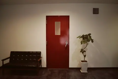 IFF STUDIO：赤い扉とソファのある通路